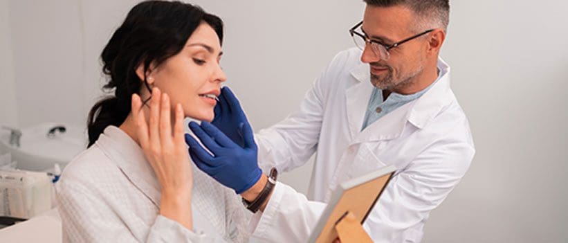 Plastic surgeon examining a female patient’s face after surgery
